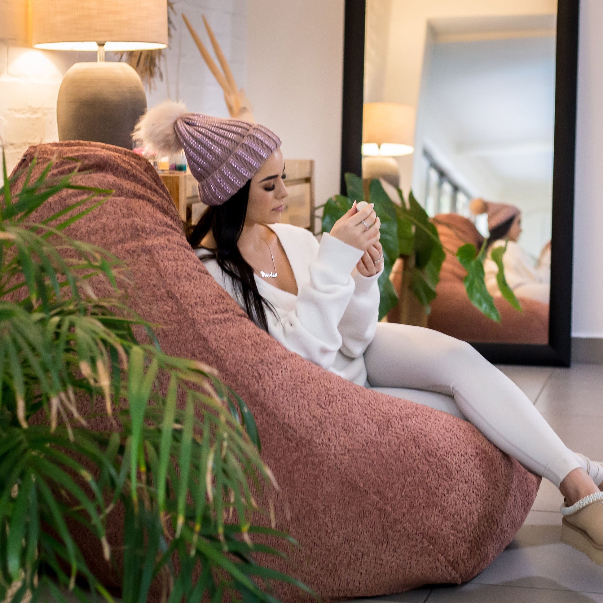 Woman sitting on a bean bag chair in a modern living room with plants and a mirror.