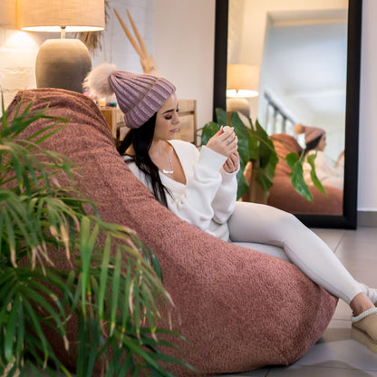 Woman sitting on a bean bag chair in a modern living room with plants and a mirror.